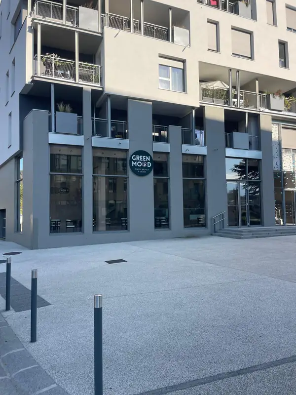 La façade : l'enseigne ronde GreenMood au rez-de-chaussée d'un immeuble, devant une esplanade piétonne.